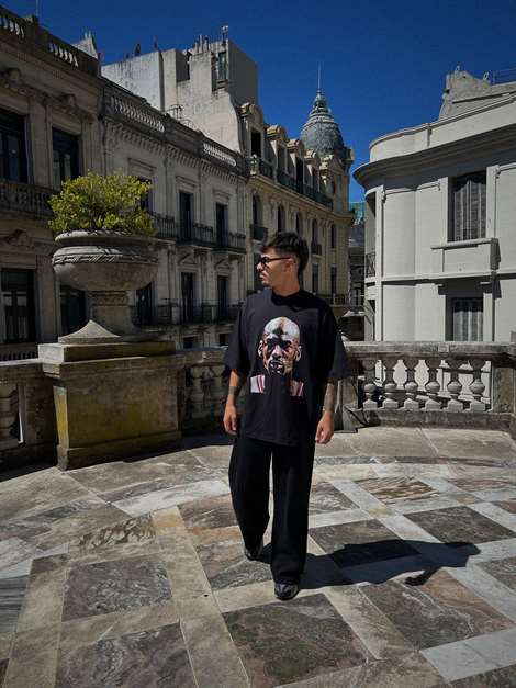 Remera negra Thairos con estampa fotográfica, caminando por una terraza.